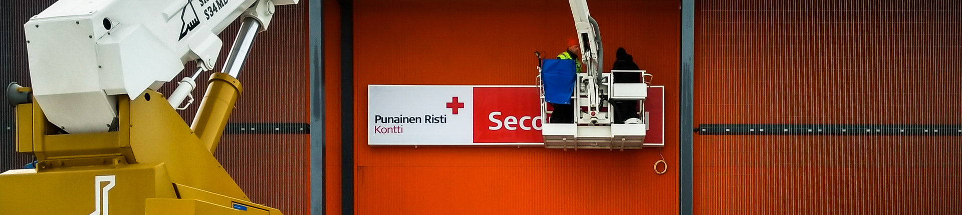 Kontti-kylttiä asennetaan nosturin kanssa rakennuksen seinään