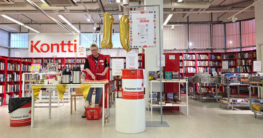 Henkilö ja kakkutarjoilut myymälässä. Taustalla iso Kontti-logo ja punaisia kirjahyllyjä.