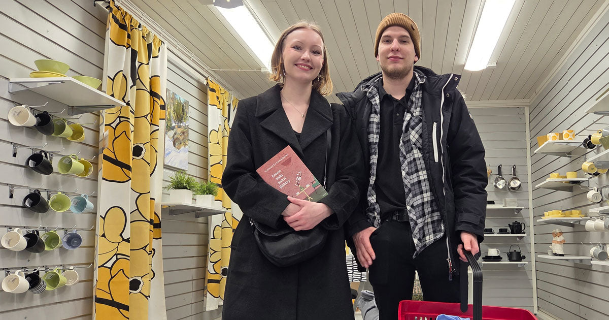 Kaksi henkilöä hymyilee kameralle, molemmilla ostoksia käsissään
