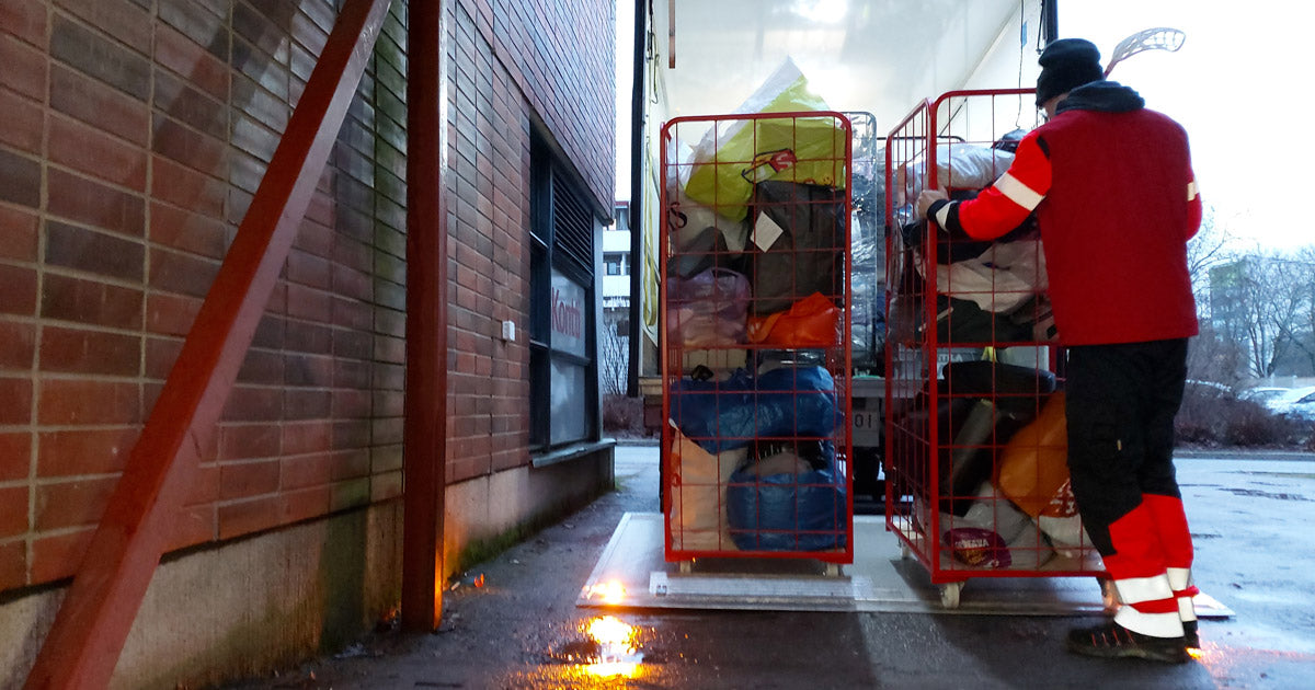 Työasuinen henkilö laskee punaisia rullakoita alas pakettiautosta.