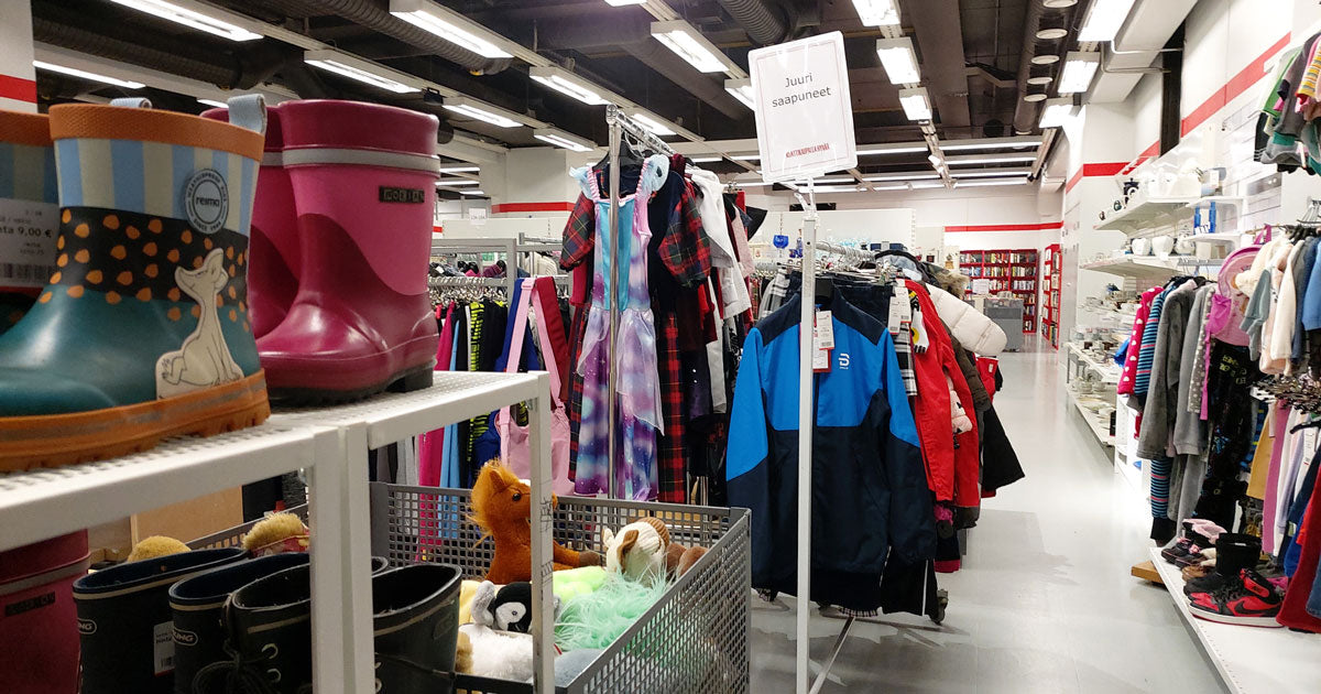 Lastenvaateosasto Kontissa. Etualalla kumisaappaita hyllyssä ja laatikollinen pehmoleluja. Vaaterekissä kyltti "Juuri saapuneet".