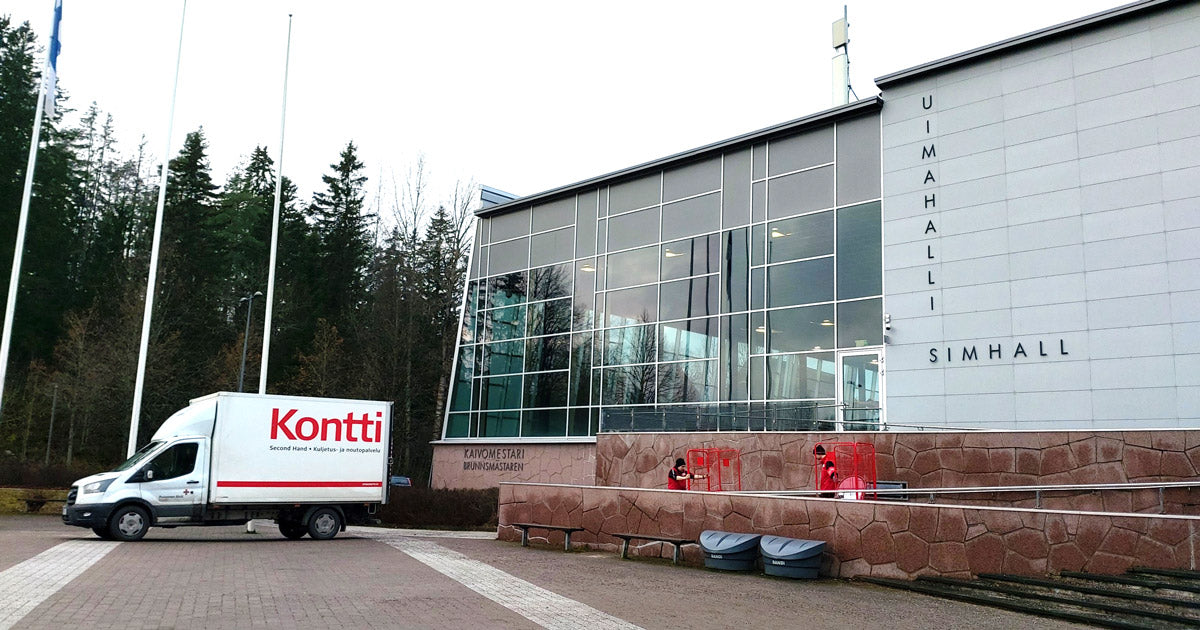 Piha-alueella Kontti-pakettiauto, johon ollaan työntämässä punaisia rullakoita. Rakennuksen seinässä luke "Uimahalli Simhall".