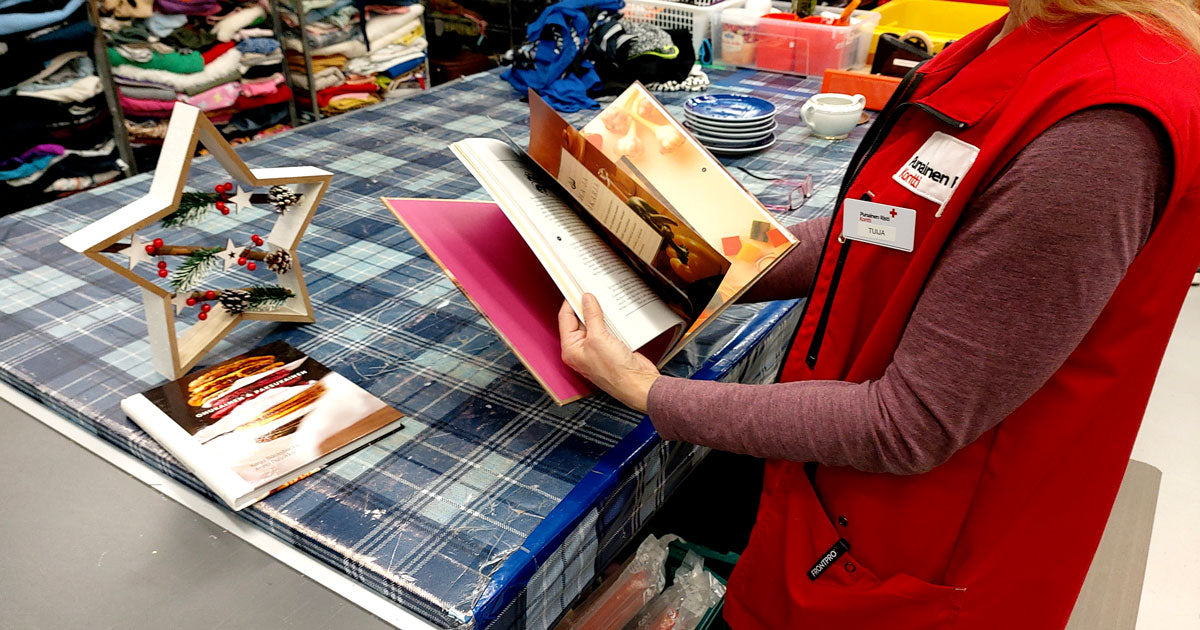 Punaliivinen työntekijä selaa ruokakirjaa Kontissa tarkastuspisteellä. Tähtikoriste odottaa pöydällä.