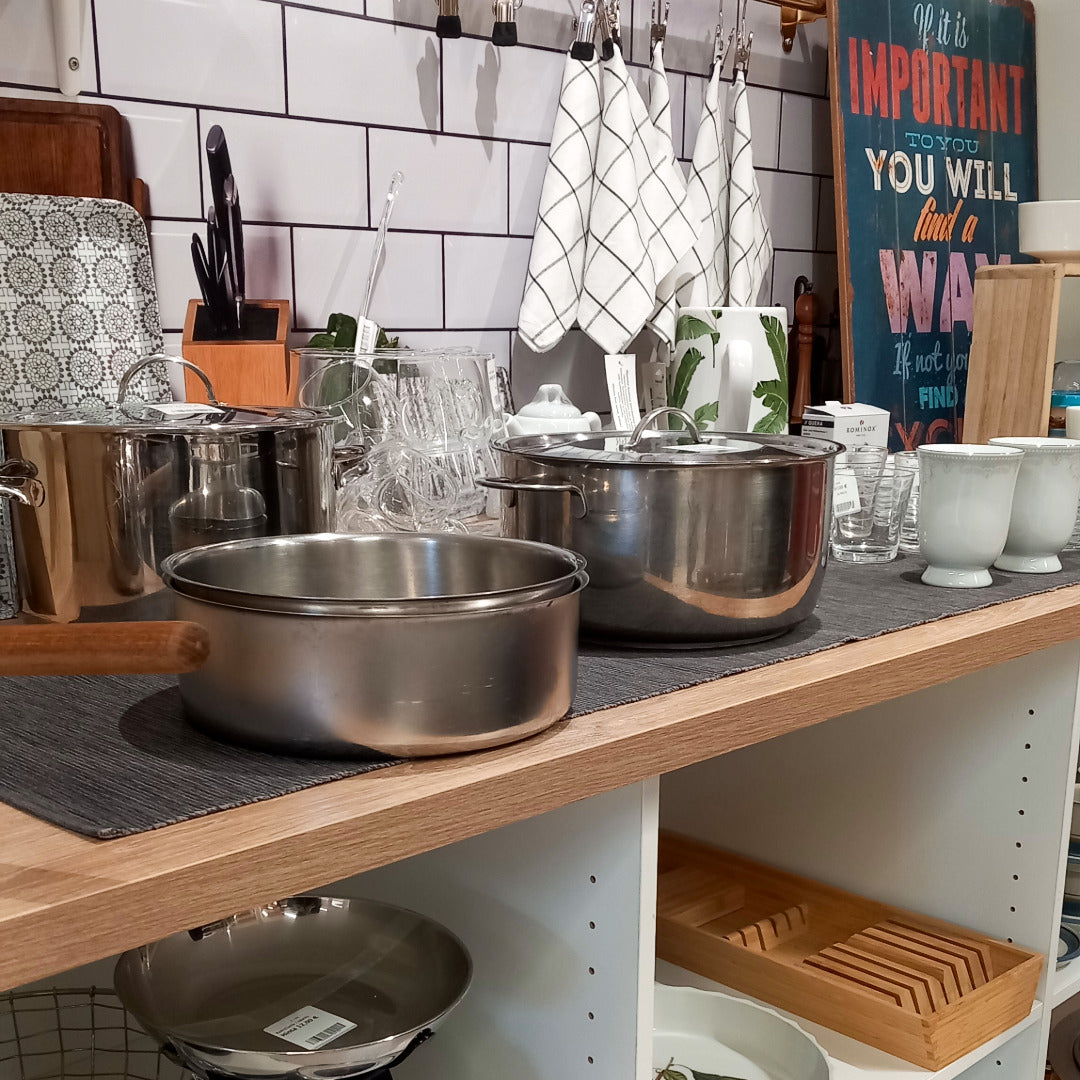 Keittiösomistus, jossa on teräskattiloita ja muuta keittiötavaraa, seinällä roikkuu ruudullisia keittiöpyyhkeitä.