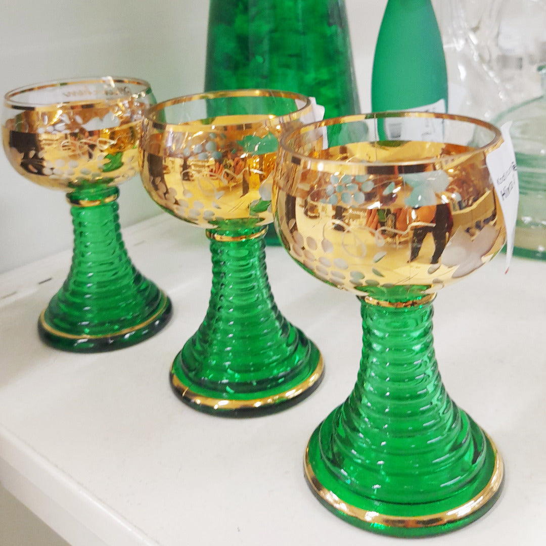 Kolme jalallista juomalaisia, joissa vihreää ja kultaa.