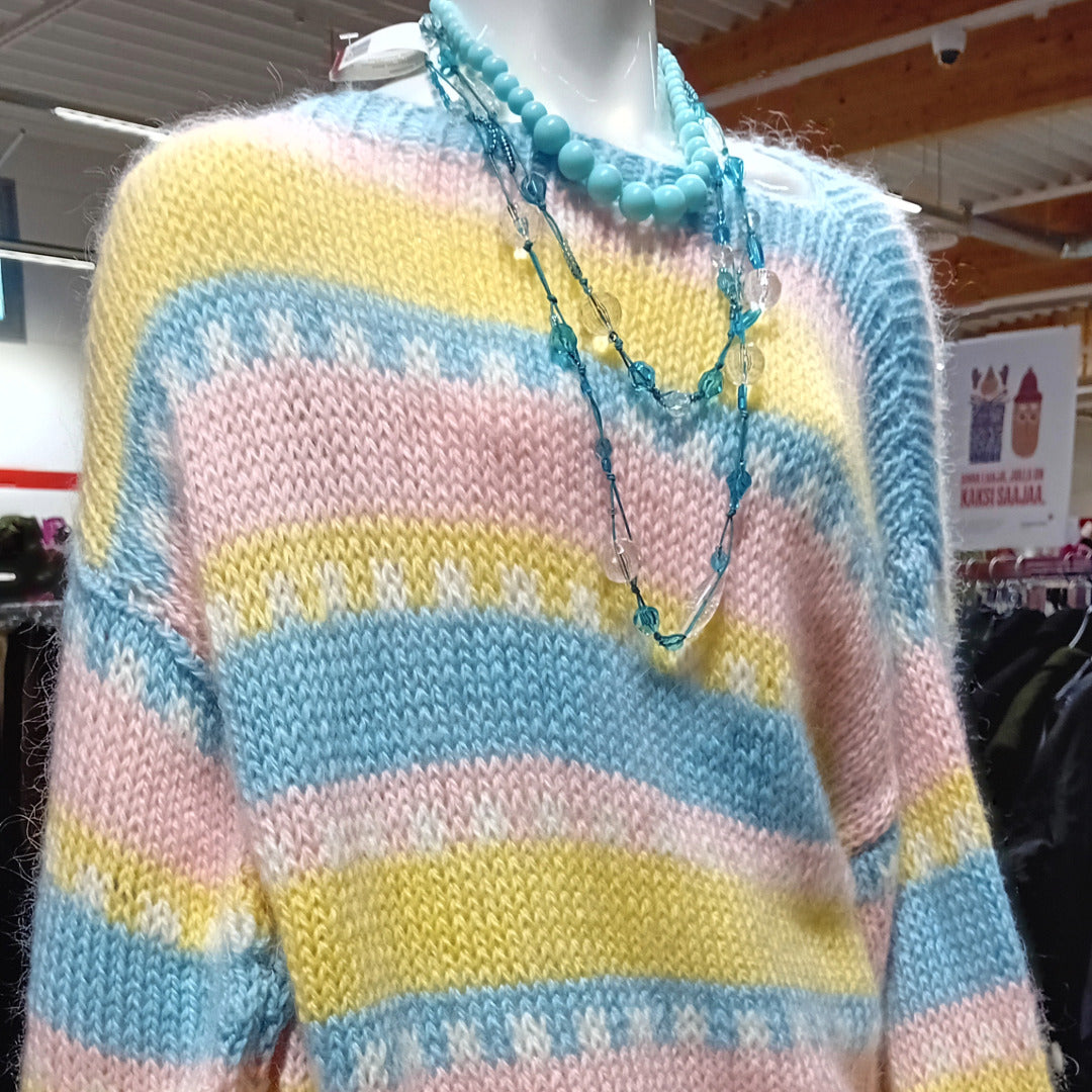 Pastellinvärinen neule ja kaulakoruja mallinuken päällä.