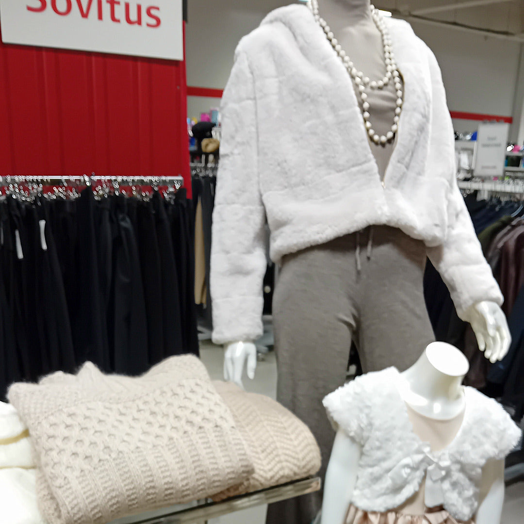 Mallinuken päällä valkoinen tekoturkisjakku ja harmaat housut. Etualalla juhlamekko lapsimallinuken päällä.