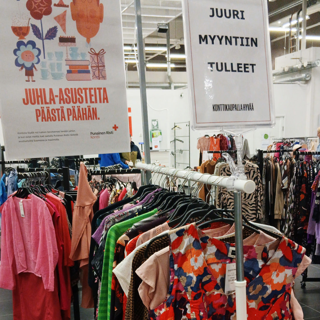 Naisten kesävaatteita rekeissä. Juliste, jossa teksti: Juhla-asusteita päästä päähän, sekä kyltti, jossa teksti: Juuri myyntiin tulleet.