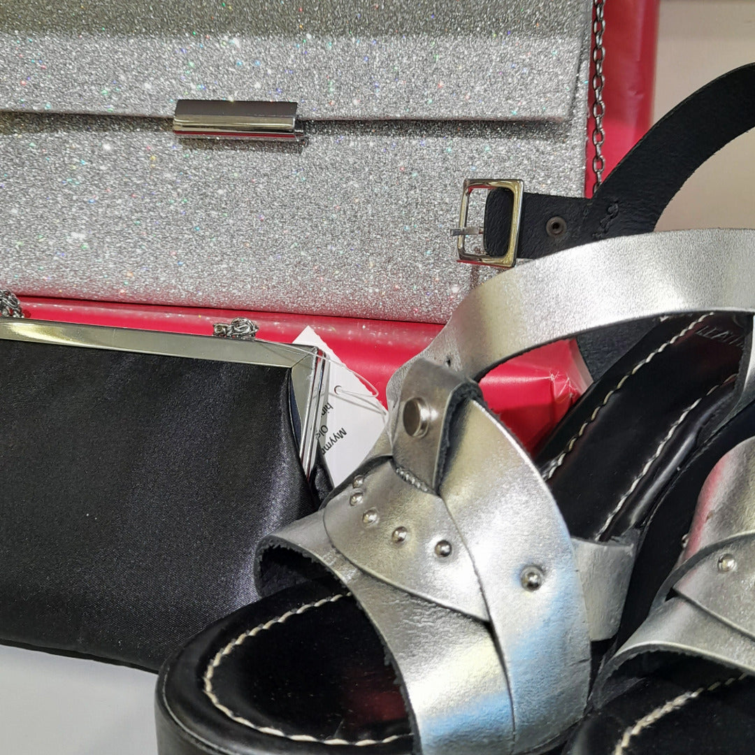 Hopeanväriset korkosandaalit sekä hopeanvärinen ja musta iltalaukku.