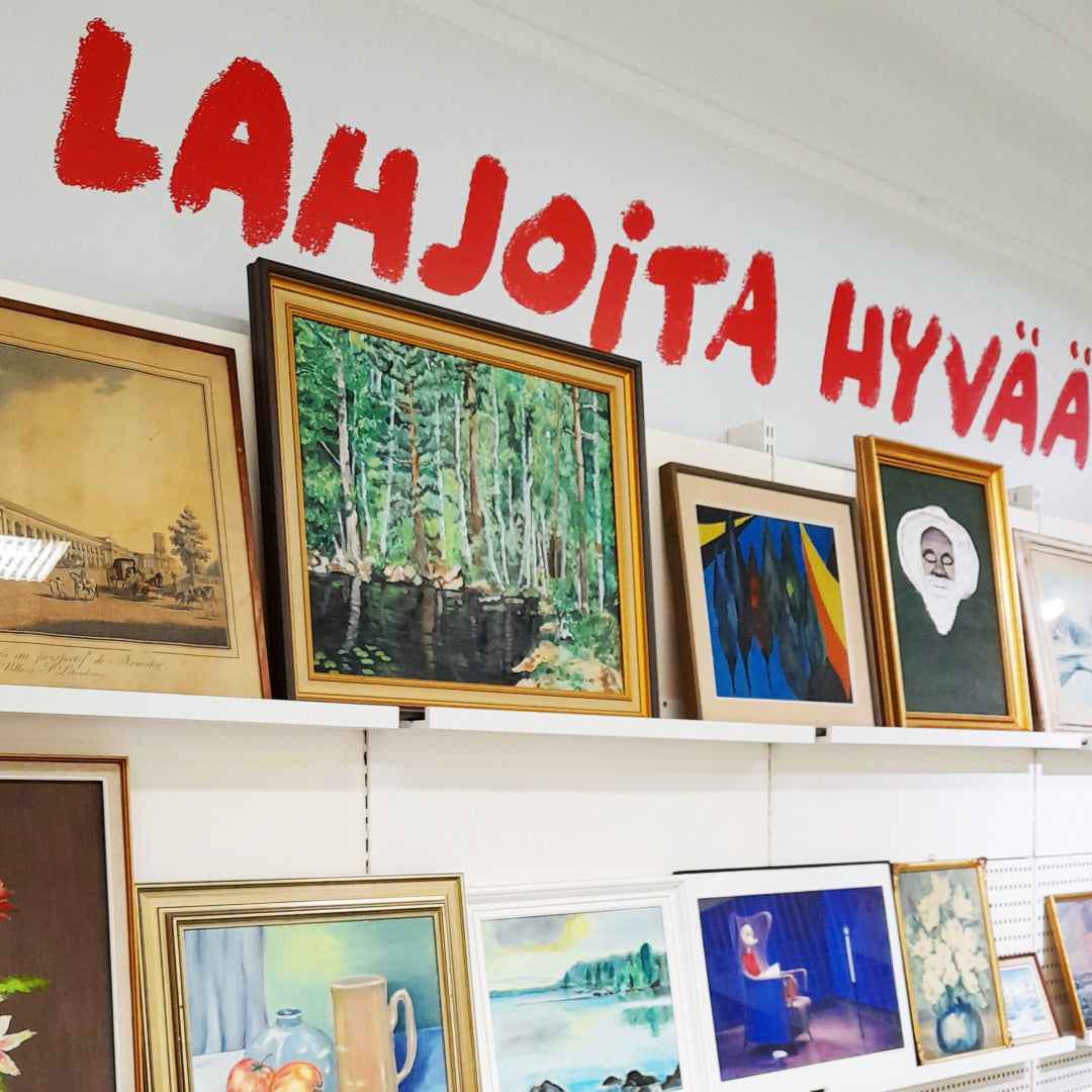 Seinällä tauluja tauluhyllyillä ja seinällä ylhäällä teksti: Lahjoita hyvää.