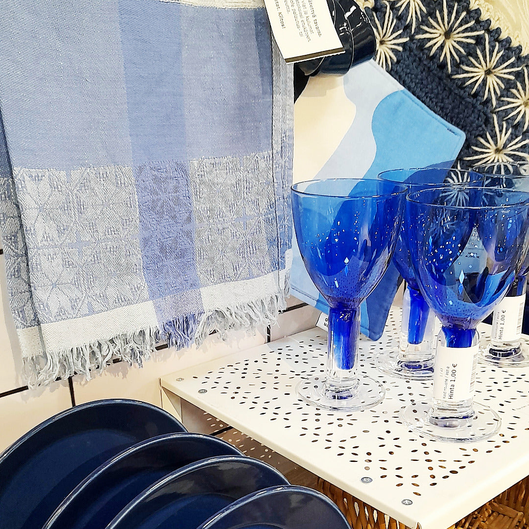 Sinisiä laseja ja lautasia sekä sinivalkoisia keittiötekstiilejä.