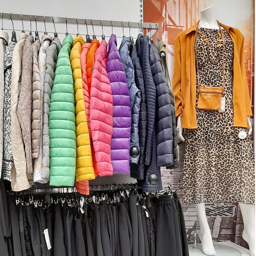 Naisten erivärisiä kevyttoppatakkeja ja mustia alaosia rekeissä, oikealla mallinukke, jolla leopardikuvioinen mekko ja oranssi takki.