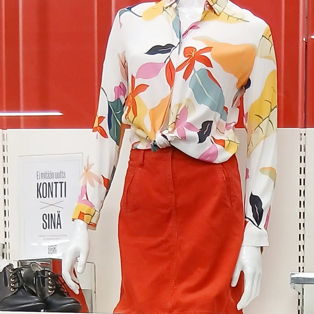 Mallinuken päällä kirjava naisten paitapusero ja punainen hame.