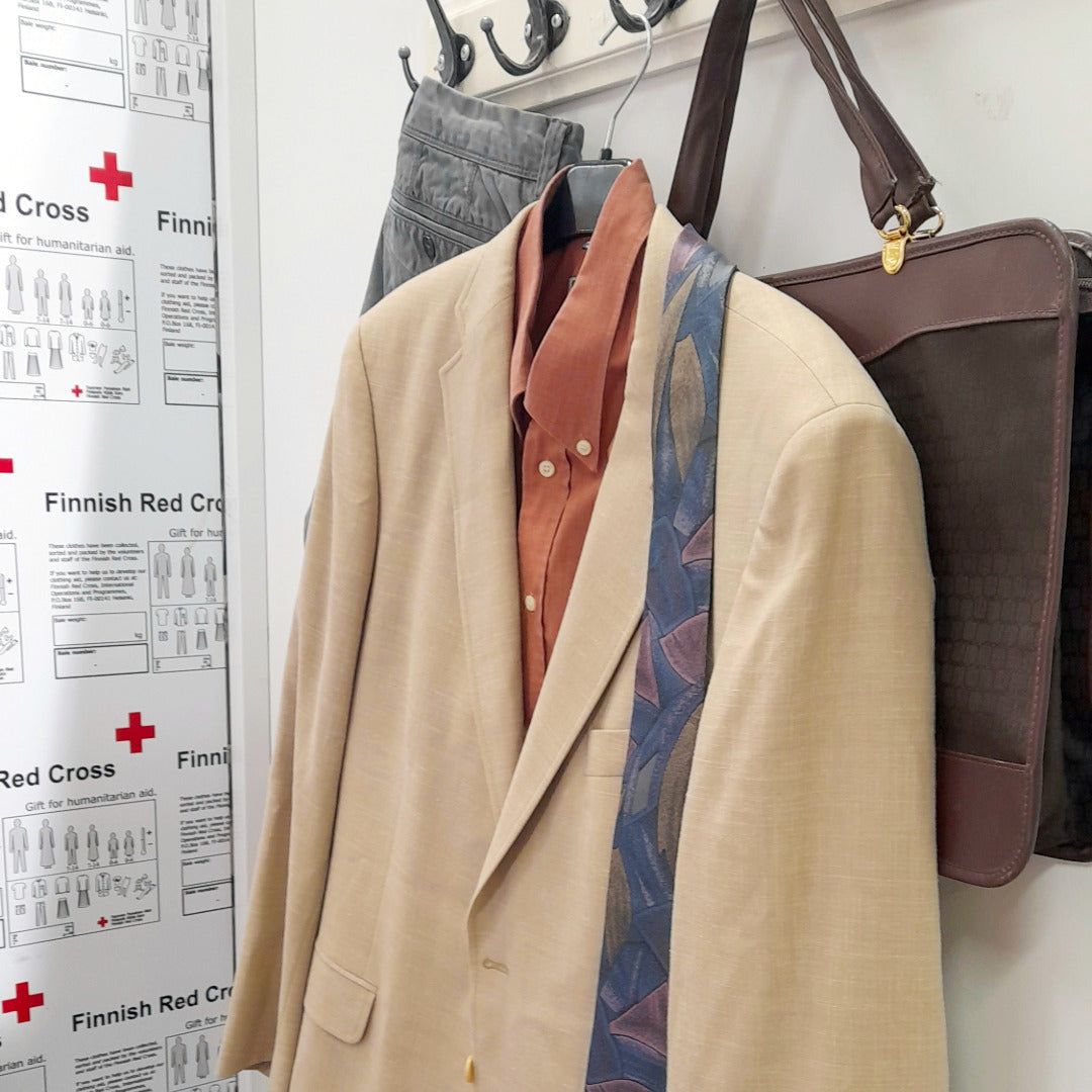 Miesten pikkutakki, paita, farkut ja salkku roikkumassa sovitusopin naulakossa.