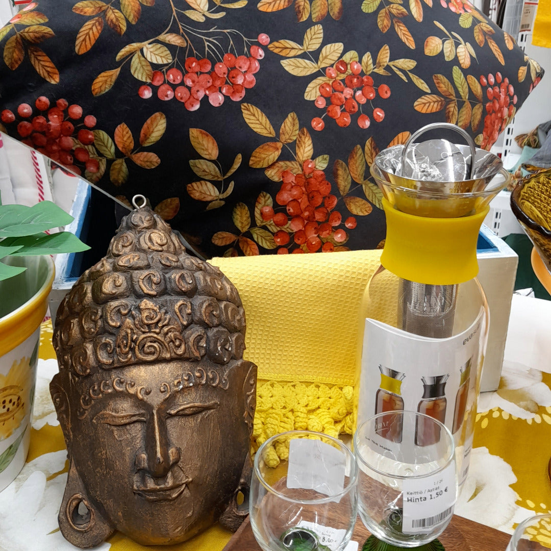 Buddha-koriste, lasikannu ja sisustustyyny pihlajanmarjakuviolla.