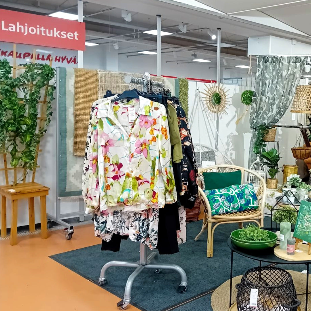 Naisten kevätvaatteita rekissä ja kevyitä huonekaluja sekä sihreäsävyistä sisustusta.